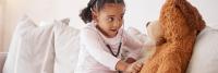 Young girl using a stethoscope to play doctor with a teddy bear.